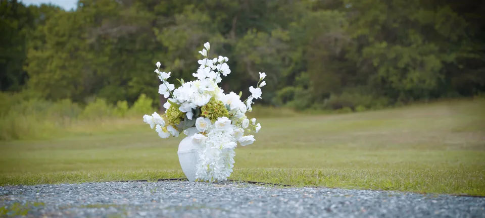 White flowers in a white vase on a gravel path across the lawn