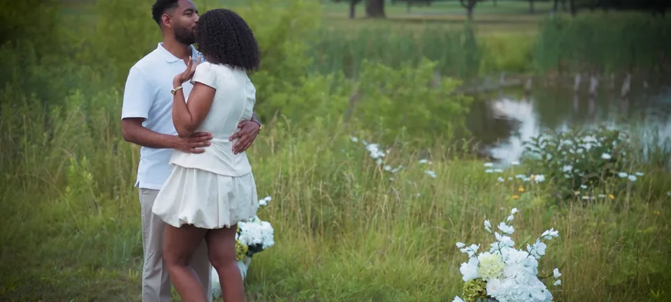 The two of them in the long grass by the pond, white flowers at their feet
