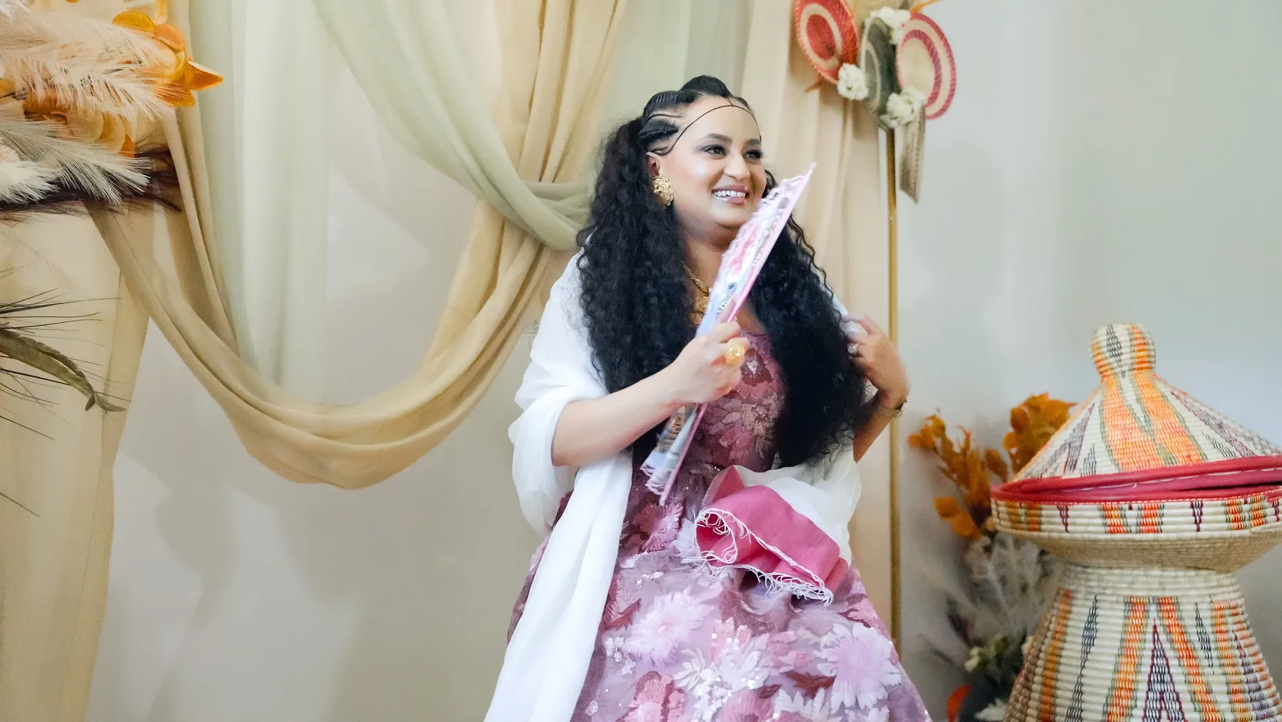 A woman holding a decorative fan, laughing, against a draped backdrop
