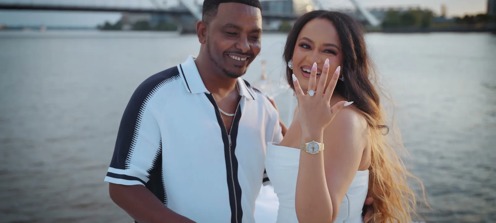 A couple at golden hour on the water, the ring just revealed