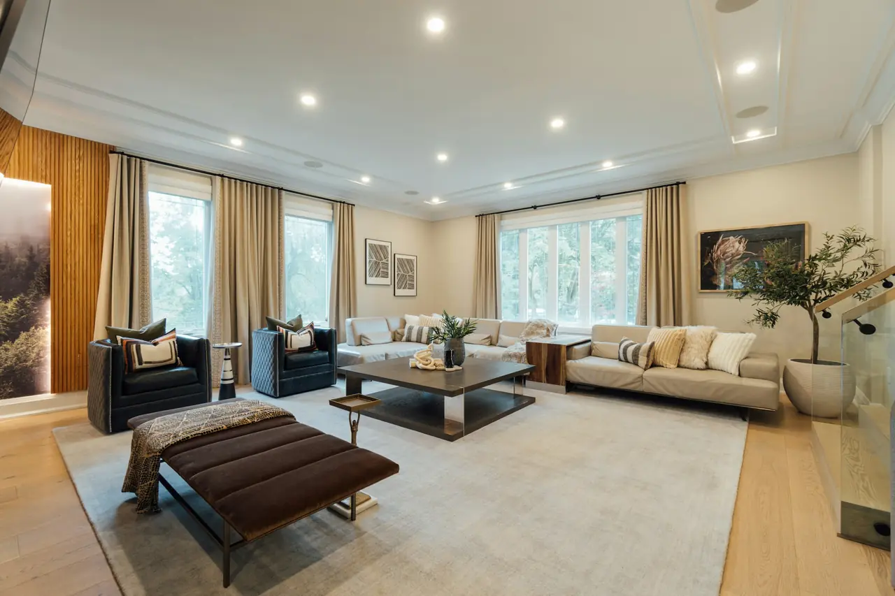 A bright living room with tall windows, recessed lights and a sectional sofa, photographed for a listing.