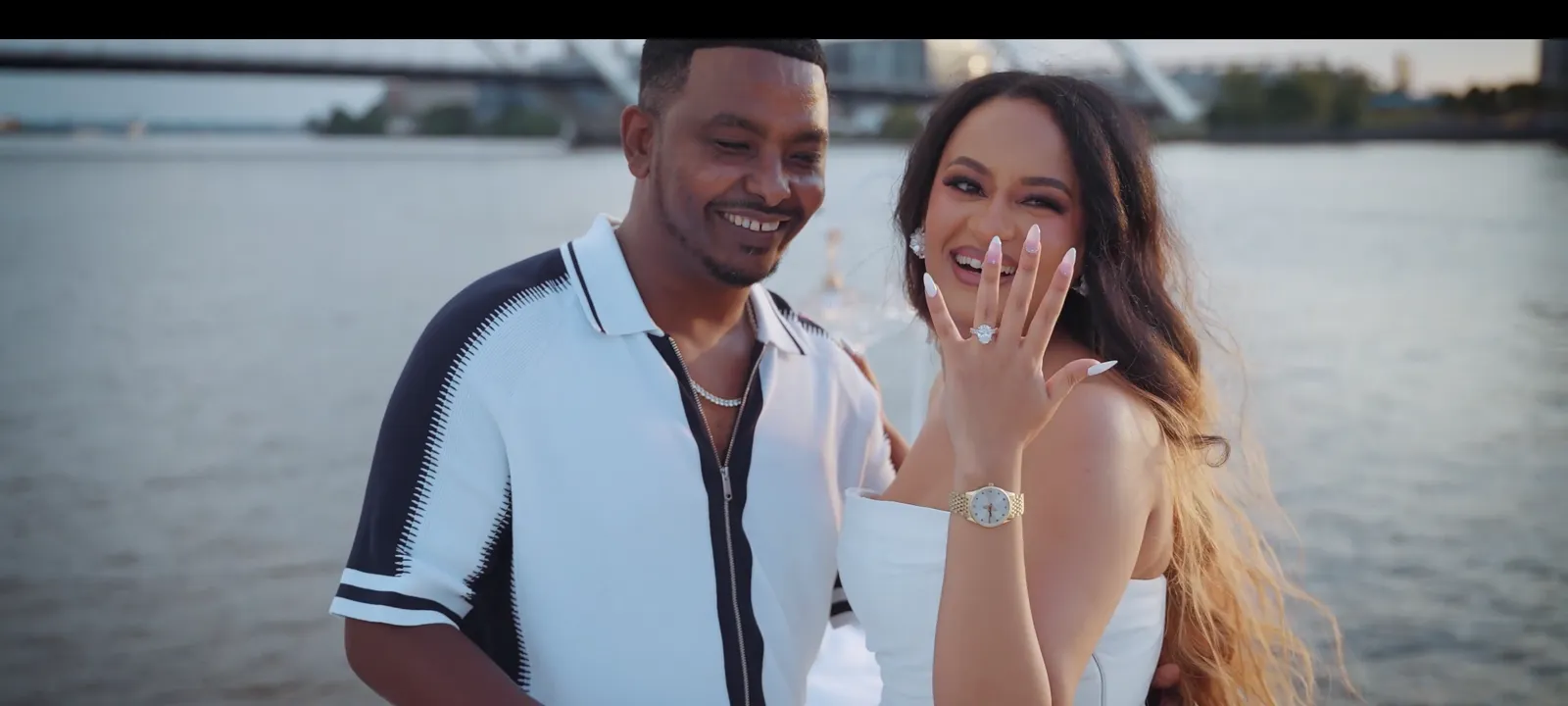 A couple at golden hour on the water, the ring just revealed